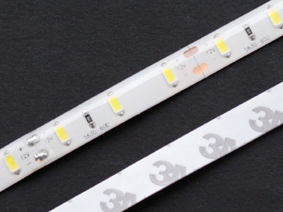 Section of ebay LED strip light (both sides). The strip is 12 mm wide. There are two groups of three LEDs (yellow). The SMD resistors are black. A splice can be seen in the lower left. The strip can be cut and new leads soldered at the copper tabs. Contrary to the logo on the back, the adhesive back is not genuine 3M quality.